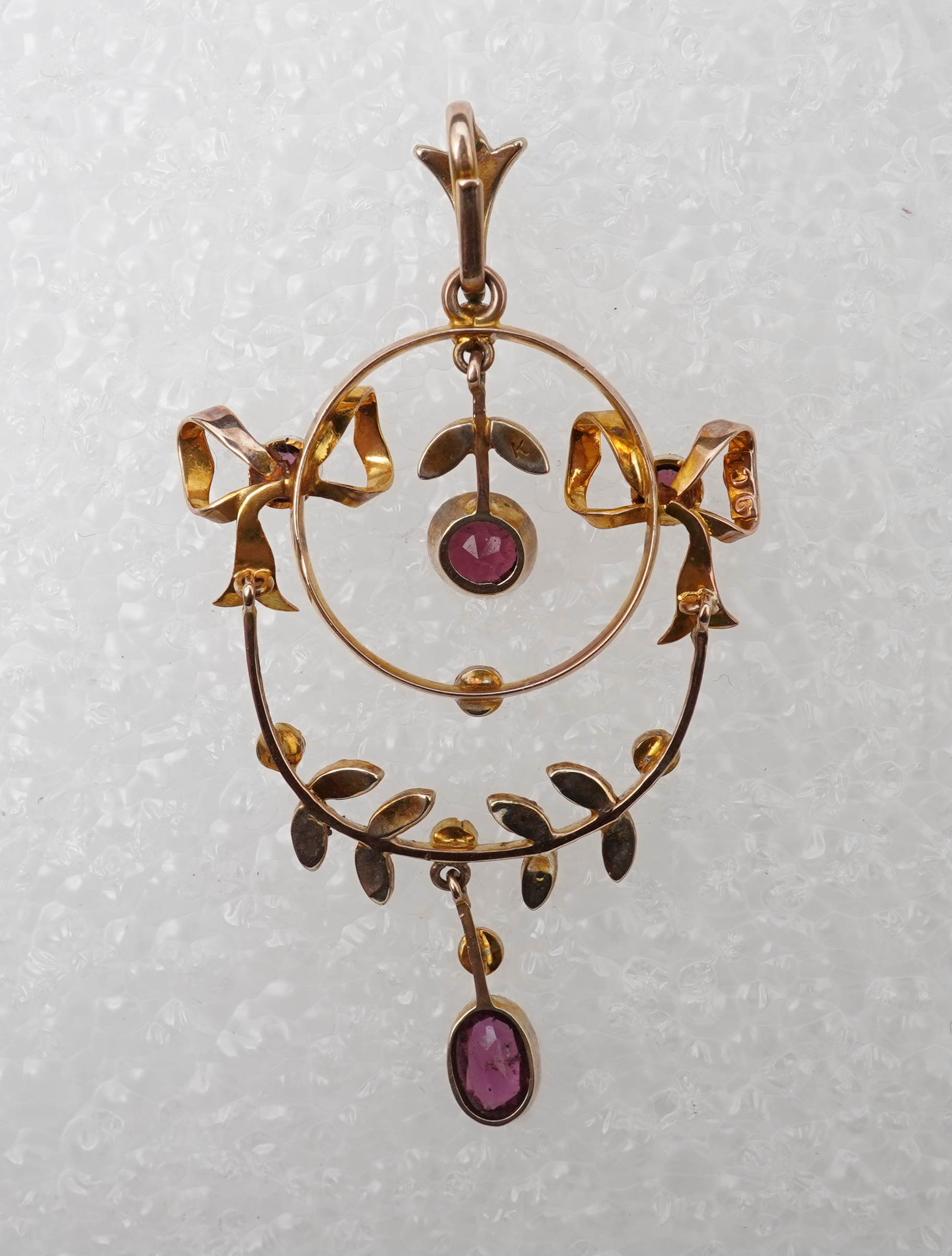 An Edwardian garnet and seed pearl pendant, early 20th century, of foliate design with ribbon bow motifs, set with circular-cut and oval garnets and seed pearls, mounted in gold, length 5.2cm, stamped 9CT, gross weight a